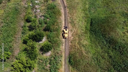 Aerial view of tractor with a cable drum laying fiber optic hawser at countryside. Workers guiding and adjusting rope to ensure proper placement under ground for communication or power infrastructure
