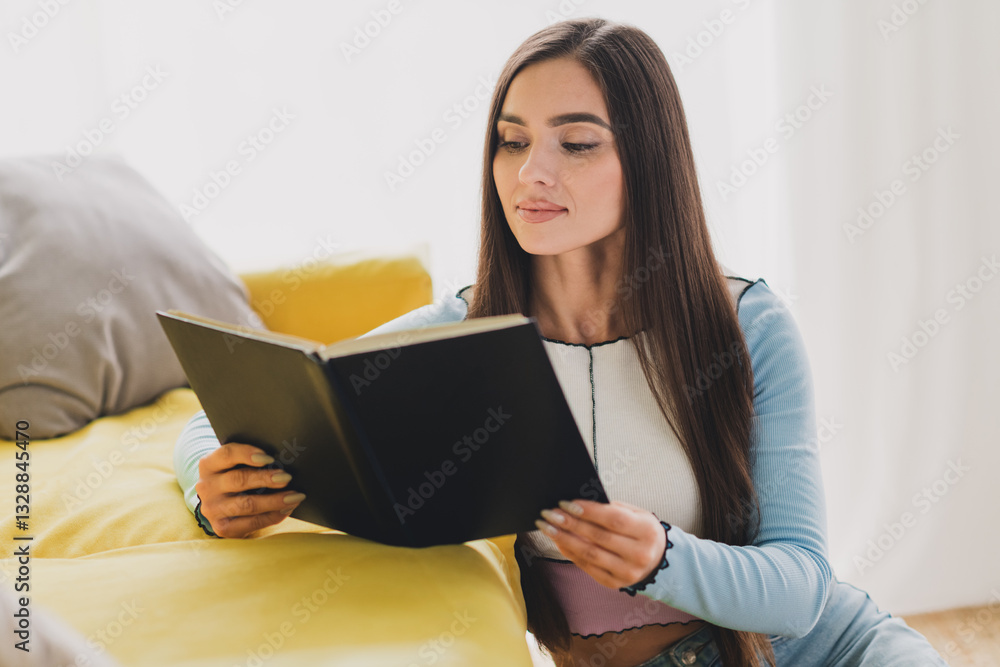 Young brunette woman reading a book while relaxing in a cozy living room with modern casual interior design and warm ambiance Young brunette woman reading a book while relaxing in a cozy living room with modern casual interior design and warm ambiance