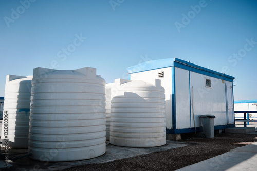 White plastic water tanks stand next to prefabricated industrial building. Newly built single storey prefabricated industrial building. Prefabricated office container building at construction site
