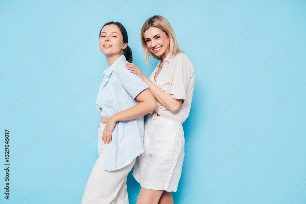 Two young beautiful smiling brunette and blond hipster female in trendy summer clothes. Lovely women posing on blue background in studio. Positive models having fun. Cheerful and happy. isolated Two young beautiful smiling brunette and blond hipster female in trendy summer clothes. Lovely women posing on blue background in studio. Positive models having fun. Cheerful and happy. isolated