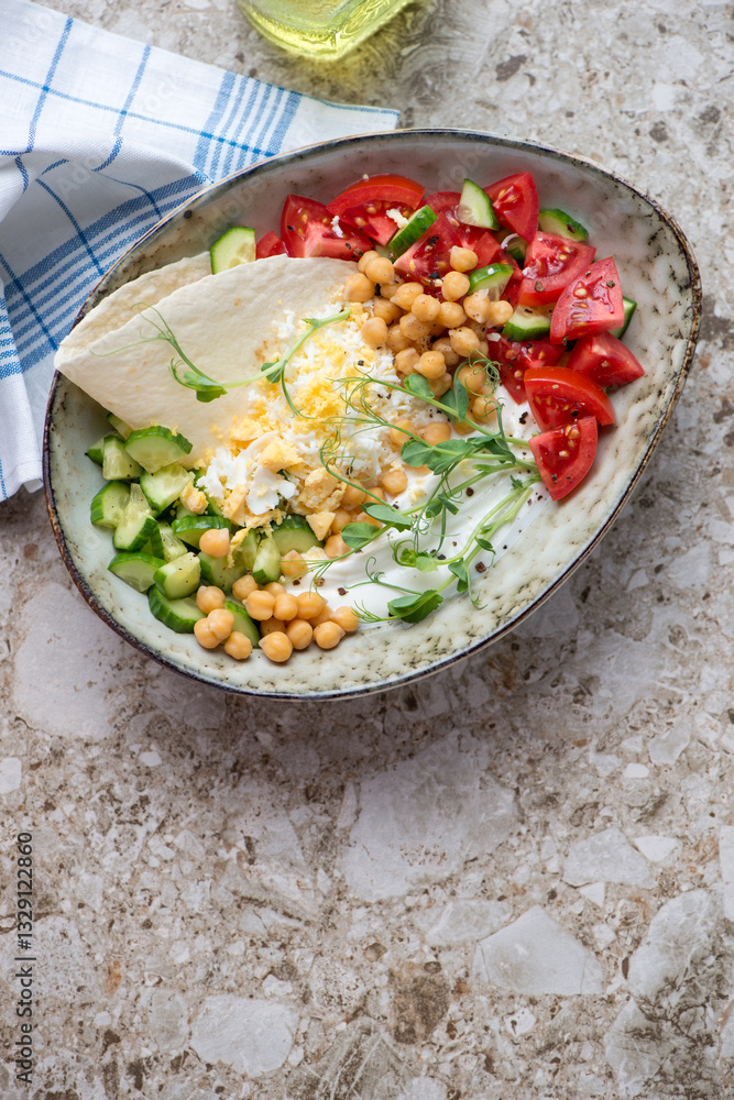 Yogurt bowl with vegetables, chickpeas, grated egg and flat bread, top view on a beige granite background, vertical shot with space Yogurt bowl with vegetables, chickpeas, grated egg and flat bread, top view on a beige granite background, vertical shot with space