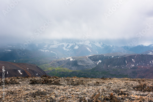 Dramatic top view from sunlit stony pass to vivid green alpine valley in sunl...