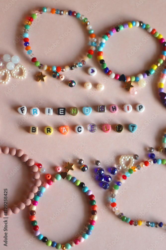 Friendship bracelet spelled with letter beads. Colorful handmade bracelets and various beads. Flat lay, pink background.