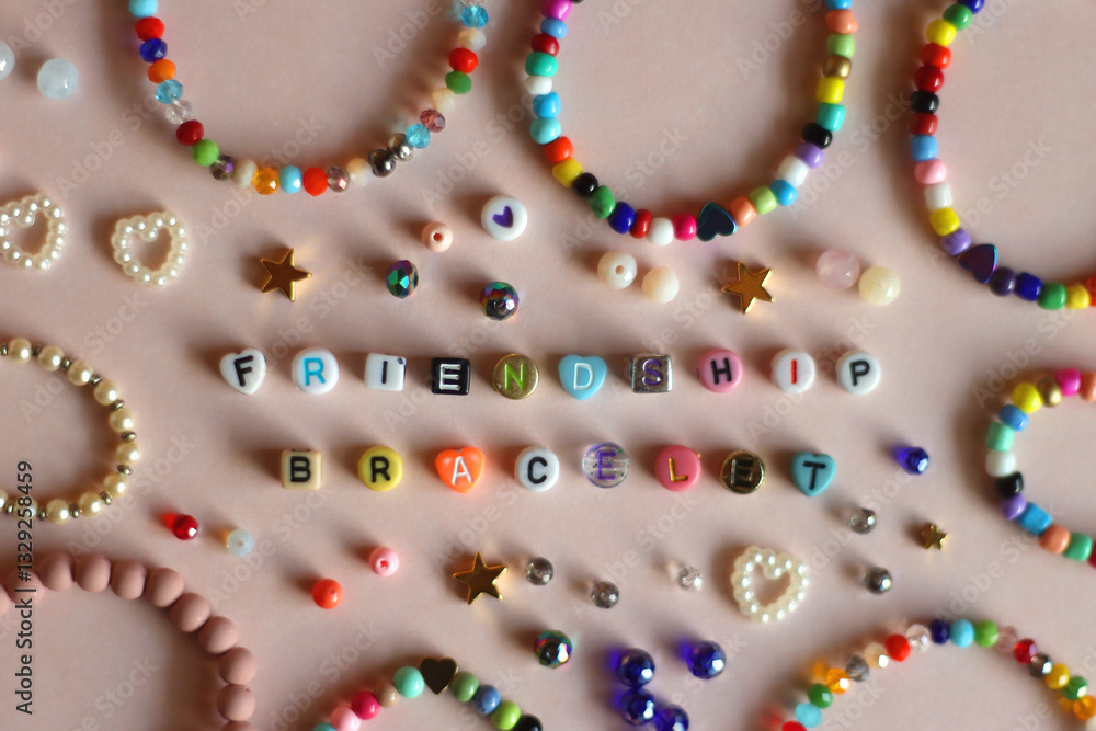 Friendship bracelet spelled with letter beads. Colorful handmade bracelets and various beads. Flat lay, pink background.