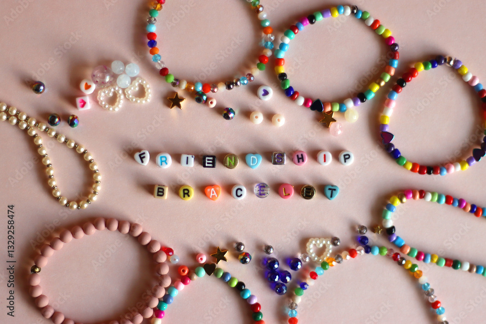 Friendship bracelet spelled with letter beads. Colorful handmade bracelets and various beads. Flat lay, pink background.
