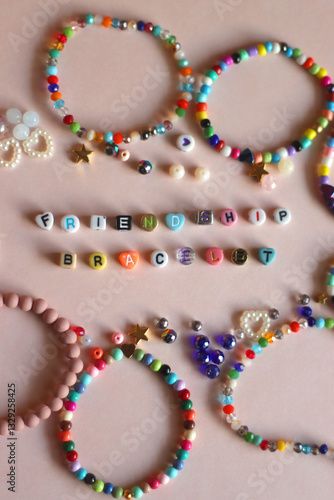 Obraz na płótnie Friendship bracelet spelled with letter beads. Colorful handmade bracelets and various beads. Flat lay, pink background. w salonie