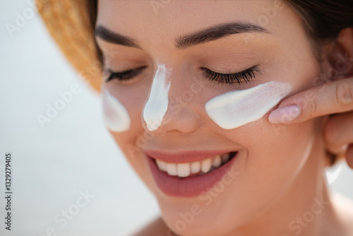 Photos A beautiful young woman enjoys a sunny day at the beach while applying sunscreen to her face