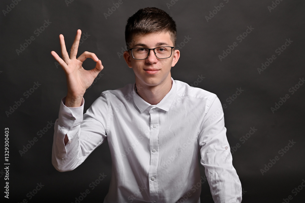 young man confidently shows an OK sign with his hand, set against simple gray background. image conveys approval, positivity, and modern, professional vibe, ideal for business or motivational themes. young man confidently shows an OK sign with his hand, set against simple gray background. image conveys approval, positivity, and modern, professional vibe, ideal for business or motivational themes.