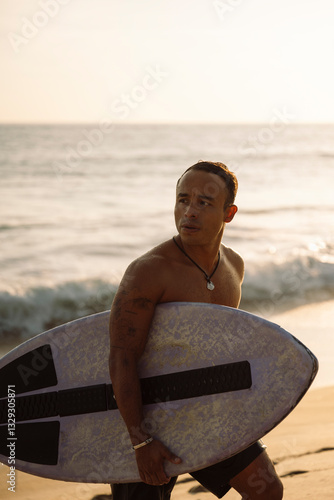 Photography Surfer walking on the beach at sunset carrying skimboard