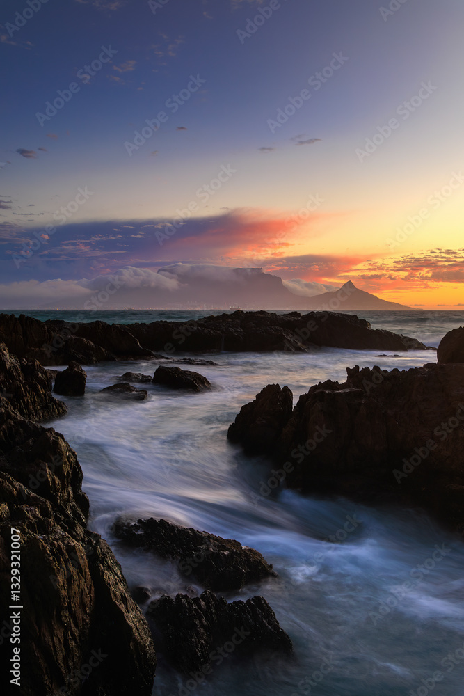 View of sunset over Table Mountain with a tranquil ocean and rocky shore, Blouberg Beach, Cape Town, Western Cape, South Africa. View of sunset over Table Mountain with a tranquil ocean and rocky shore, Blouberg Beach, Cape Town, Western Cape, South Africa.