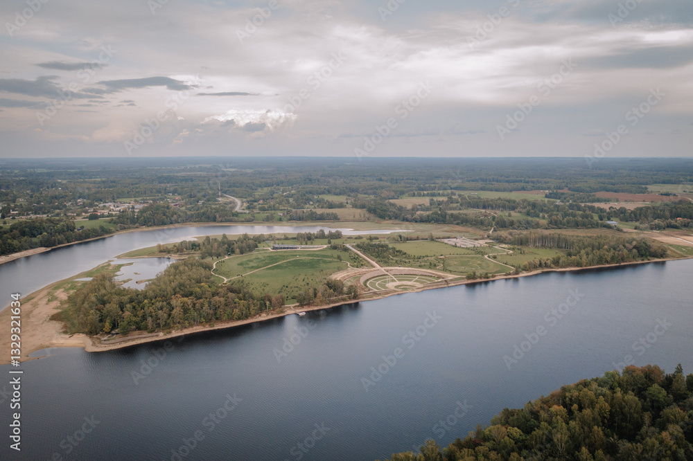 Aerial view of a scenic riverside landscape featuring green fields, winding paths, a modern park design, and a calm river under a cloudy sky.. Aerial view of a scenic riverside landscape featuring green fields, winding paths, a modern park design, and a calm river under a cloudy sky..