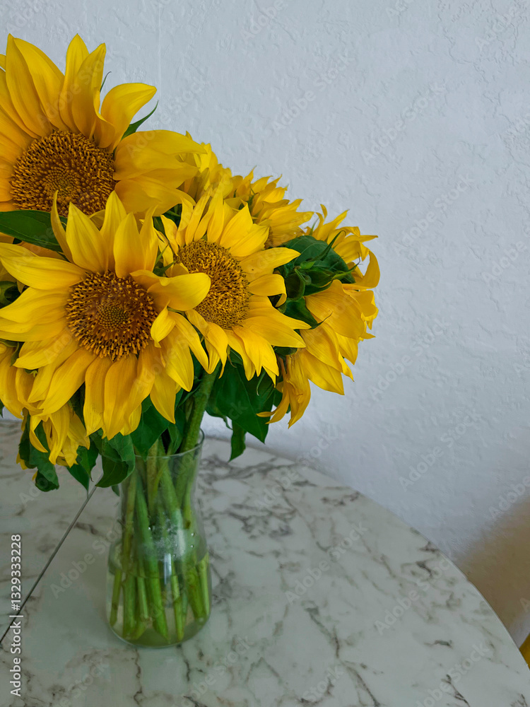 A bouquet of sunflowers stands in a glass vase on a marble table in a white kitchen