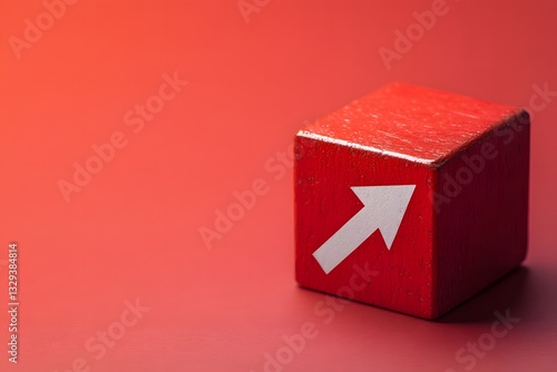 Red wooden block with arrow symbol pointing upward on a solid red background in a minimalist setting