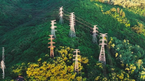 Sunset Illuminates High Voltage Power Line Tower Atop Mountain Surrounded by Lush Greenery