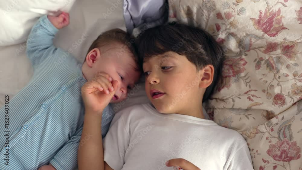 Baby and older brother lying together on bed, sharing affectionate moment, baby reaching towards sibling, bonding in peaceful home setting, warmth and sibling connection