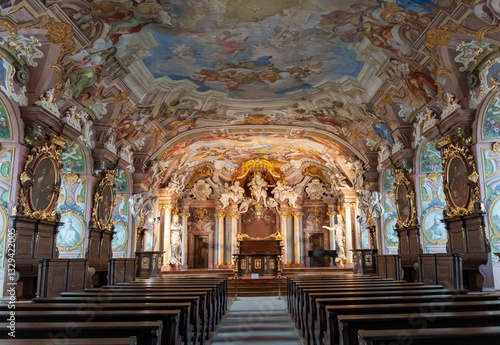 Baroque church interior with stunning frescoed ceiling, golden altar, and ornate decorations. Rows of wooden pews lead to the altar, emphasizing the grandeur of sacred architecture.