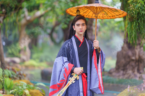 Chinese warriors wearing old traditional costumes. An elegant warrior in a conventional blue robe holding a sword wearing a woven bamboo hat in the forest. Ancient Chinese warrior portrait.
