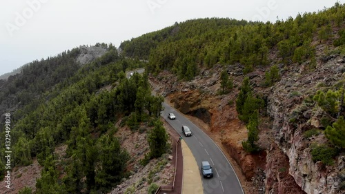 Aerial view of beautiful volcanic landscape with highway and cars driving along forest and rocks. 4K drone video. Heights of Volcano Teide, Tenerife, Canary islands, Spain. Footage above cloud level
