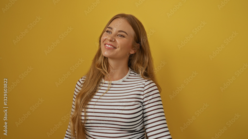 Fototapeta premium Young woman smiling in front of a yellow background showing her attractive features and blonde hair while wearing a striped shirt.