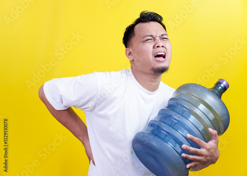 An asian man struggling to carry a heavy water gallon, holding his back in pain, expressing discomfort.