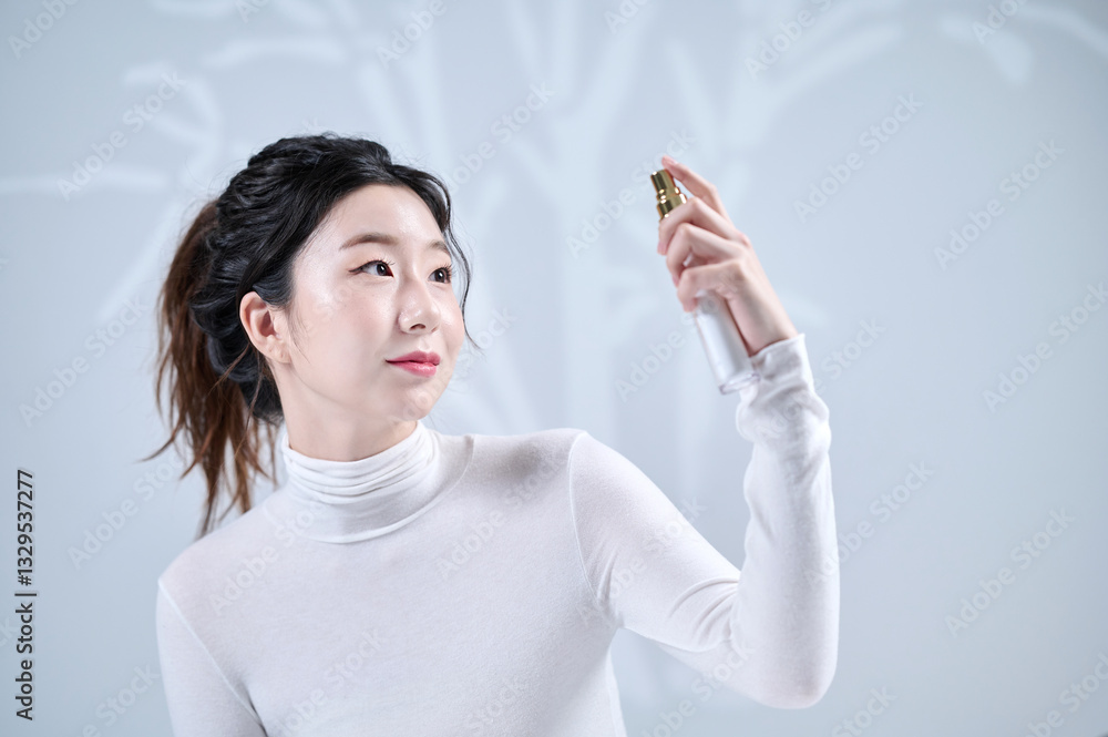 A young, beautiful Asian girl sprays her face with spray-type cosmetics in front of a wall with a shadow of a tree A young, beautiful Asian girl sprays her face with spray-type cosmetics in front of a wall with a shadow of a tree