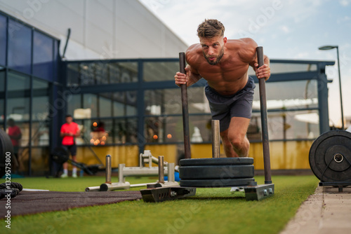 Photography Muscular sportsman performing intense physical exercise with weighted sled on a