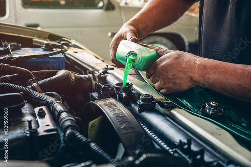 Male professional mechanic pouring antifreeze coolant liquid into car engine radiator in service center, car repair shop. Concept of car radiator coolant maintenance