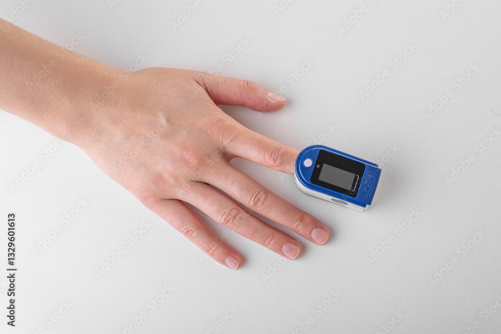 A close-up image of a person's hand with a blue and white pulse oximeter clipped onto their fingertip, used to measure oxygen saturation and heart rate.