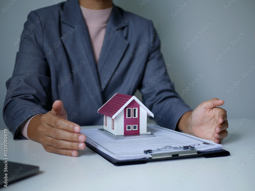 A young real estate agent covers a small house model and insurance with her hands. Renting and buying a house concept. A young real estate agent covers a small house model and insurance with her hands. Renting and buying a house concept.