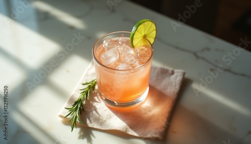 Refreshing pink cocktail with lime garnish and rosemary sprig on marble countertop in bright sunlight