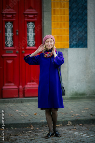Obraz na płótnie A woman in a stylish coat and beret standing on a street near a traditional Portuguese house, blending modern elegance with classic surroundings. w salonie