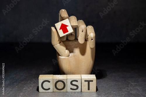 sztuczna ręka trzymająca kostkę z czerwoną strzałką w górę nad napisem na kostkach: COST. Koncepcja poprawy rentowności poprzez obniżanie kosztów.