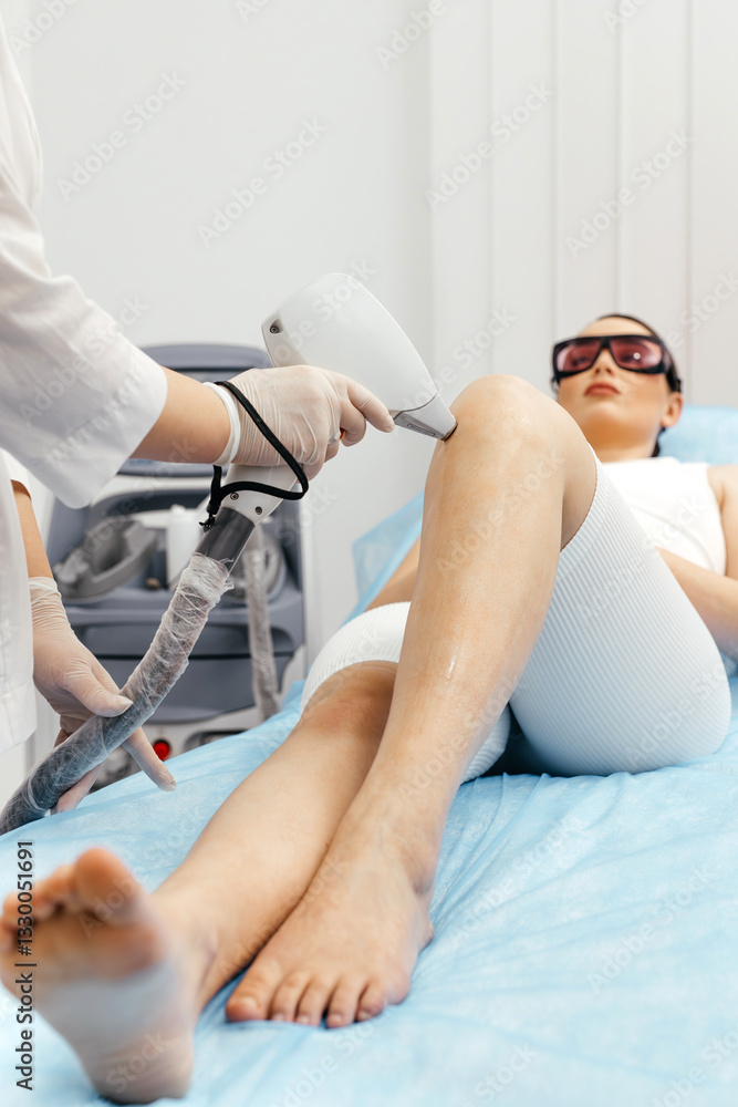 Obraz premium A young woman enjoys a close-up laser hair removal treatment on her legs in a modern beauty salon. Concept of highly effective technology and client comfort in a stylish spa setting.