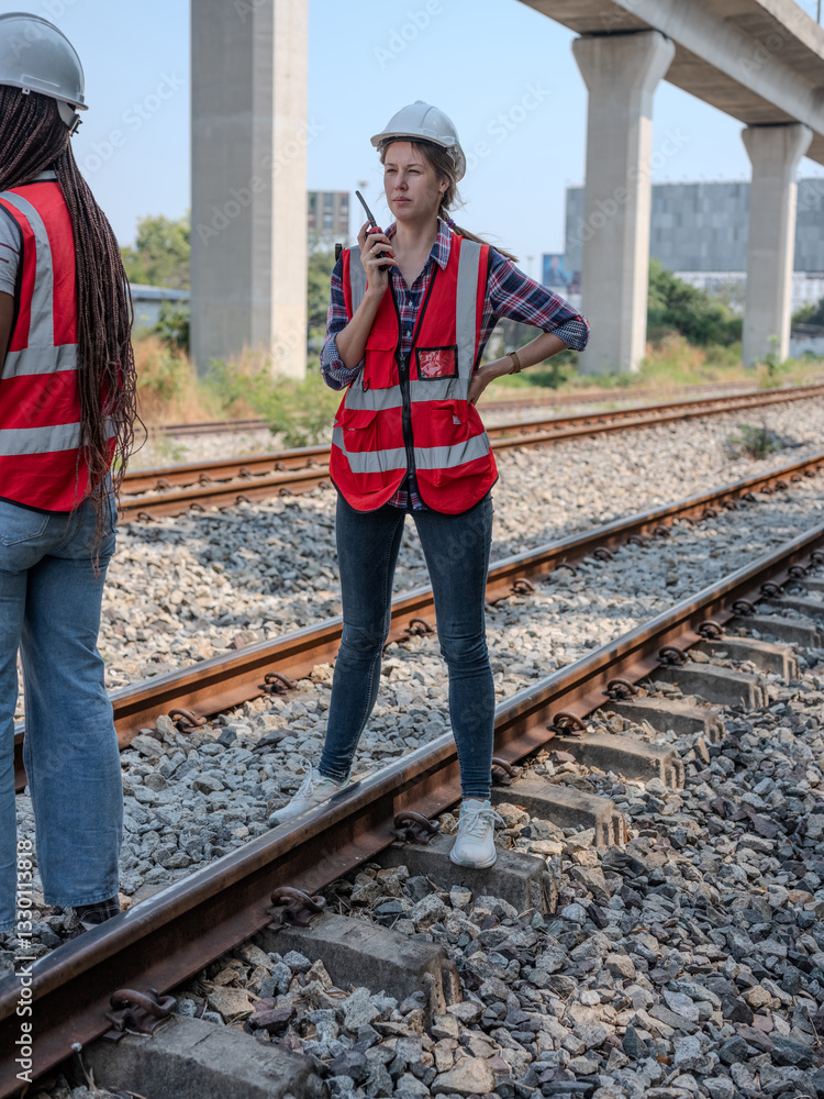 Female railway engineer discusses problems, coworker agrees to the proposal, tells coworker to look at and use radio communication to talk to maintenance staff at construction site.