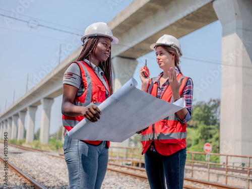 Obraz na płótnie A female railway engineer discusses problems with her colleagues and uses a radio to talk to maintenance personnel at the construction site. w salonie