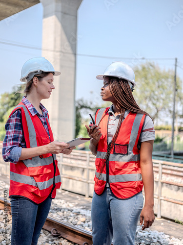 Multi-ethnic female engineers as they inspect the operation of a railway station using  a digital tablet and a walkie-talkie.
