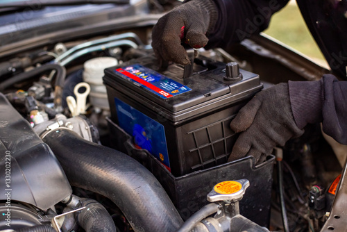 Replacing a car battery. A man installs a battery in a box under the hood of a car