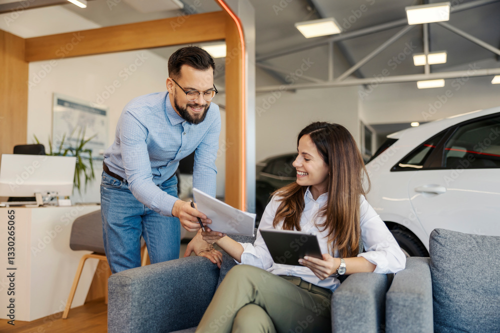 Obraz premium Friendly smiling car dealer standing at car showroom and giving a contract to a female buyer.