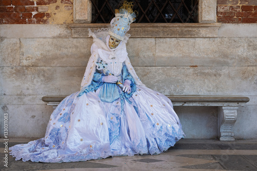 Elegant female carnival mask seated on a bench in Venice
