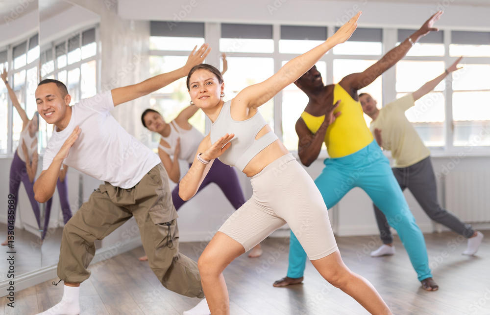 Naklejka premium Cheerful emotional sporty young female dancer rehearsing popping techniques during group workout in modern street dance studio