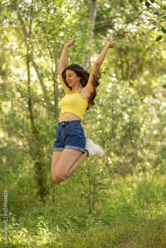 Cuadro en lienzo Una joven salta con alegría en un bosque, con los brazos en alto, disfrutando de un día soleado