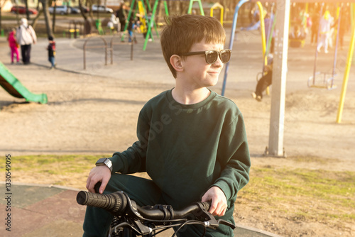 Child on a bike with sunglasses in a park during golden hour, with trees in the background. Great for illustrating active kids or serene outdoor scenes.