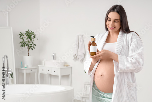 Young pregnant woman with bottle of cream in bathroom photo