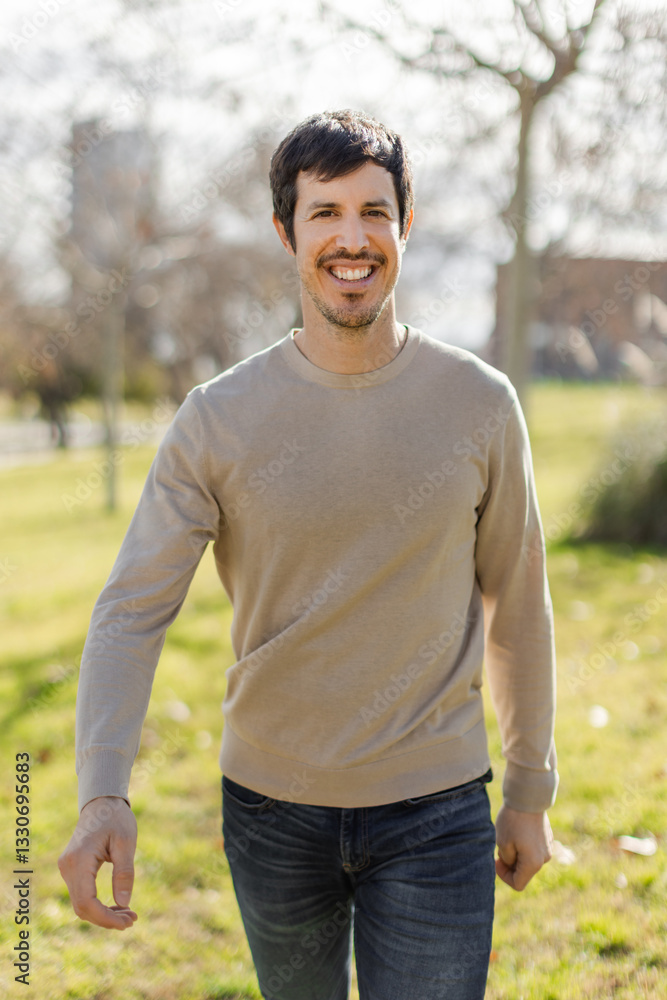 A cheerful middle-aged Caucasian man walks through a sunlit park, smiling warmly looking at camera. The natural light and greenery create uplifting atmosphere. Vertical image, blurred background. A cheerful middle-aged Caucasian man walks through a sunlit park, smiling warmly looking at camera. The natural light and greenery create uplifting atmosphere. Vertical image, blurred background.