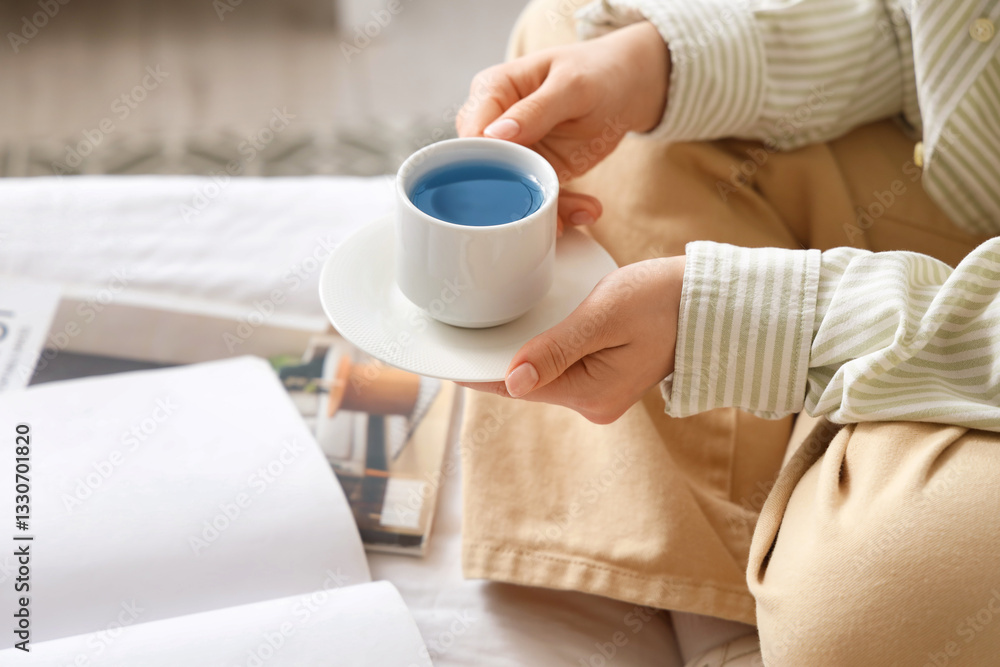Woman with cup of blue tea on bed at home, closeup