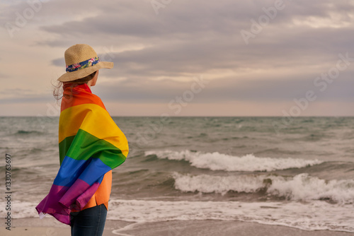 Standing Proud by the Shore, a Person Embraces the Vibrant Spectrum of Love and Unity at Twilight on the Beach
