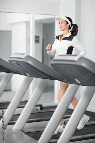 Принти на полотні Pretty young woman running on treadmill in brightly lit gym
