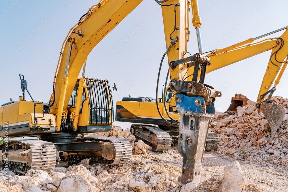 Yellow crawler excavator digs stones next to a drilling machine in a quarry Yellow crawler excavator digs stones next to a drilling machine in a quarry