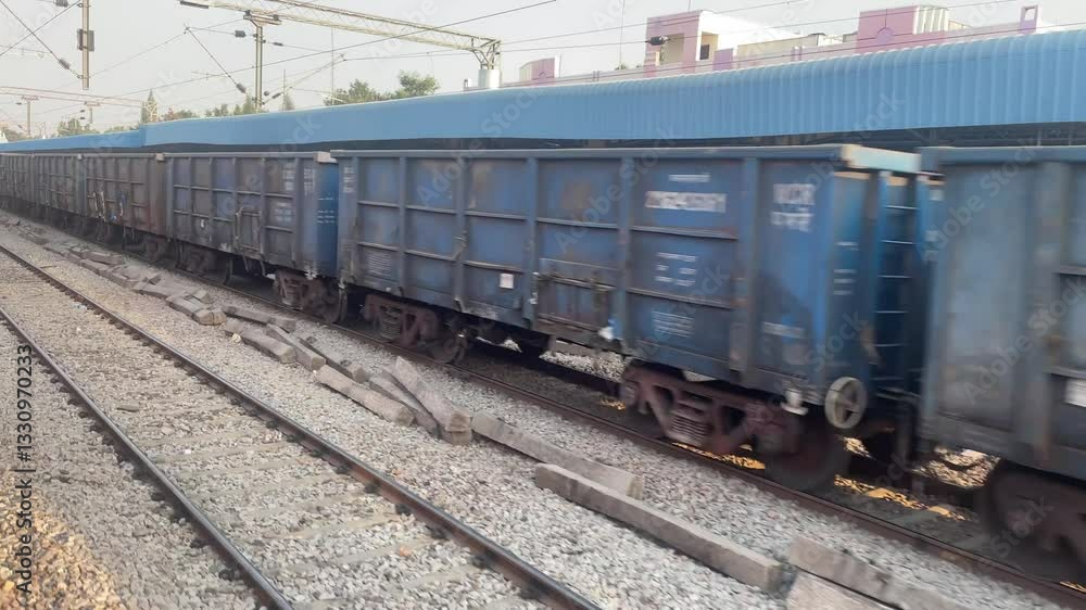 Blue Freight Train with Open Wagons on Parallel Railway Tracks in Industrial Setting Blue Freight Train with Open Wagons on Parallel Railway Tracks in Industrial Setting