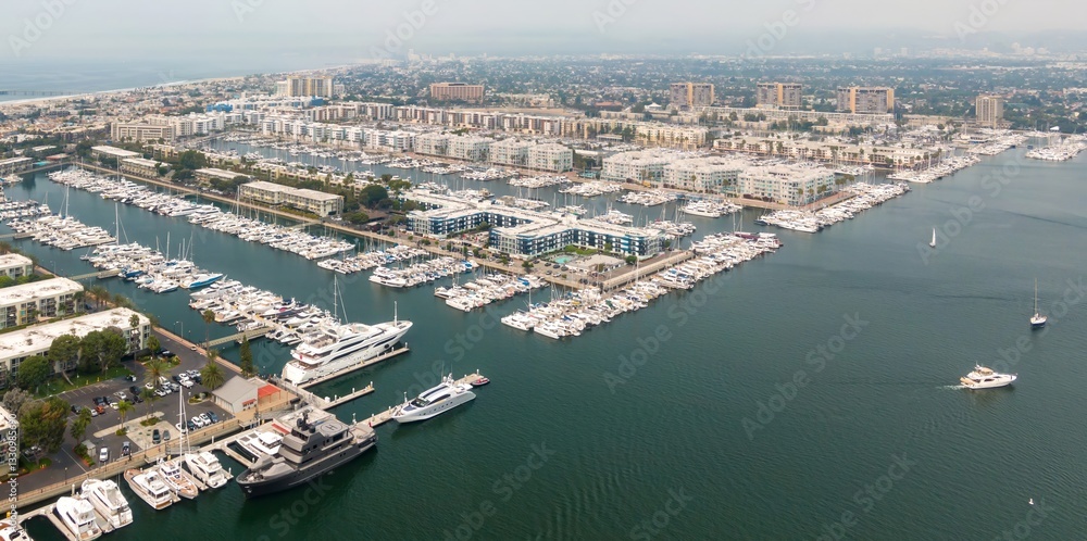 Naklejka premium Aerial view of Marina del Rey, California, USA, showcasing a dense harbor filled with yachts and boats docked along piers. Condos and buildings line the waterfront.